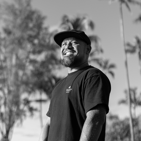 Man wearing a black cap and t-shirt with a logo, standing outdoors with trees in the background