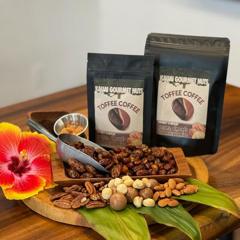 Kauai Gourmet Nuts toffee coffee with a scoop of nuts on a wooden board, surrounded by tropical flowers.