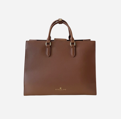 A brown leather tote bag with dual top handles and a small gold logo on the front, photographed against a plain light gray background.
