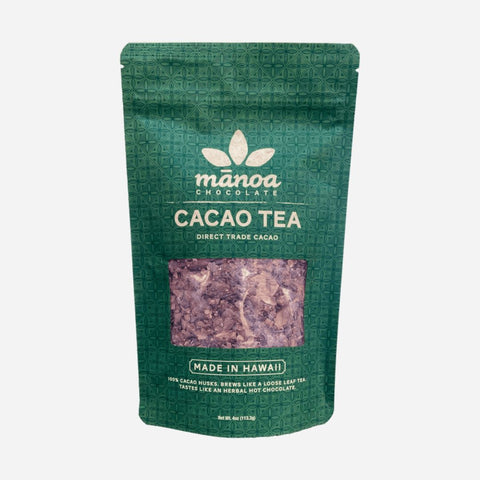 A green pouch of Manoa Chocolate Cacao Tea with a clear window showing the product inside, labeled 'Made in Hawaii'.