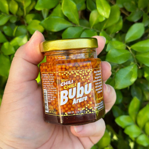 Hand holding a jar of Bubu Arare chili product against a green leafy background
