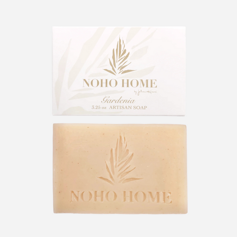 A bar of soap with 'NOHO HOME' branding and a floral design, accompanied by a packaging card with the same branding and the word 'Gardenia' indicated.