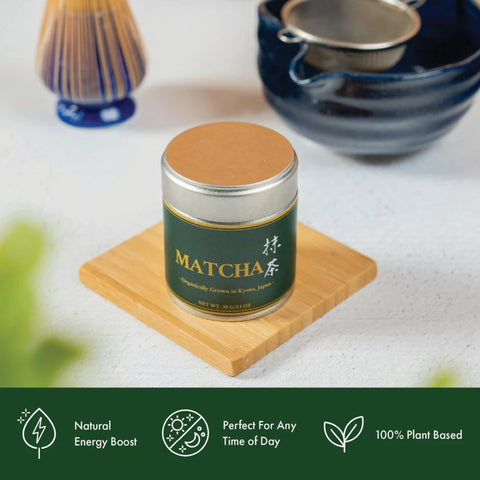Matcha tea canister on a wooden coaster with tea-making tools in the background