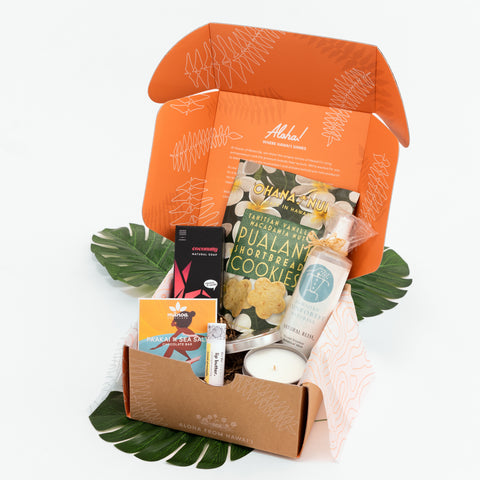 Open gift box with various items including a candle, cookies, and skincare products on a white background.