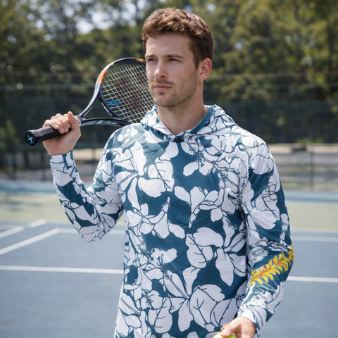 Man holding a tennis racket on a tennis court wearing a floral hoodie