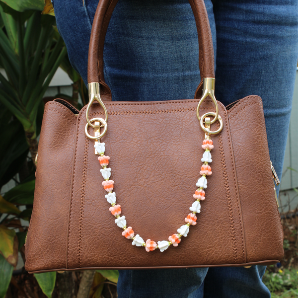 Brown handbag with decorative handle chain held by a person wearing blue jeans.