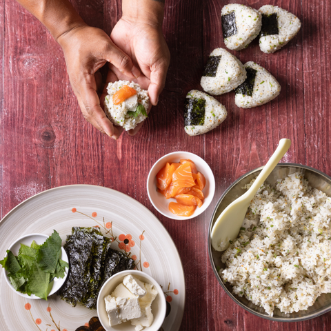 Hands making sushi on a wooden table with ingredients and tools.