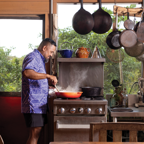 Man cooking in a kitchen with pots and pans hanging above him