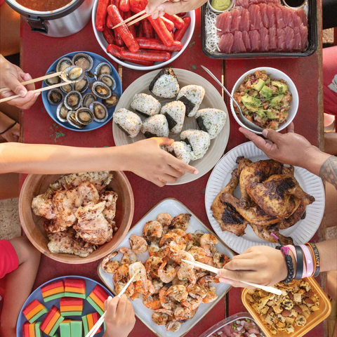 Diverse array of food on a table with people using chopsticks to eat.