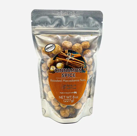 A 3 oz stand-up pouch of Cinnamon Spice Roasted Macadamia Nuts, showing the nuts inside through a clear window on a light gray background.