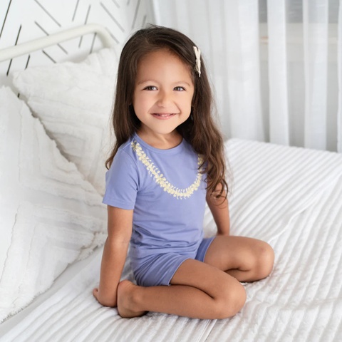 Young girl in a blue outfit sitting on a white bed
