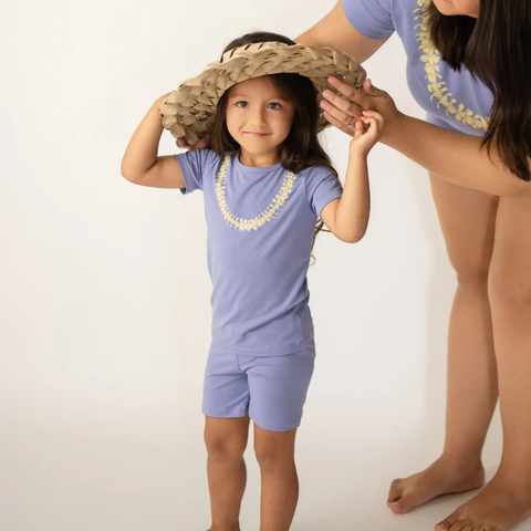 Child wearing a blue outfit with a hat and lei, standing next to an adult on a white background
