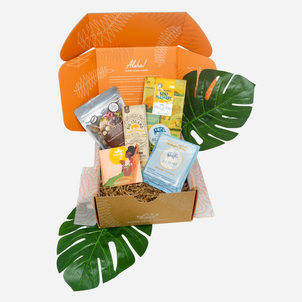 An open orange subscription box filled with assorted packaged snacks and tea, styled with green monstera leaves on a light gray background.
