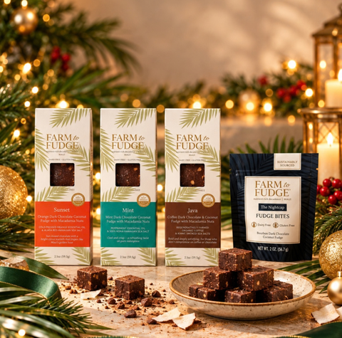 Four Farm to Fudge packaged chocolate products are displayed on a rustic table with holiday lights and pine branches in the background. The set includes three boxed varieties—Summer, Mint, and Java—and one dark pouch of Fudge Bites, with several chocolate squares arranged on a plate in front.