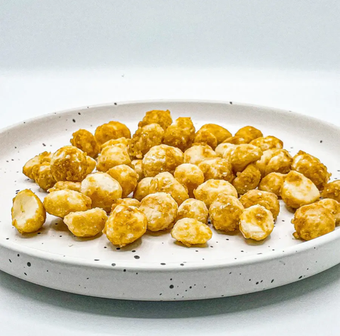 Crispy golden-brown fried snack bites or popcorn pieces piled on a speckled white ceramic plate against a clean white background.