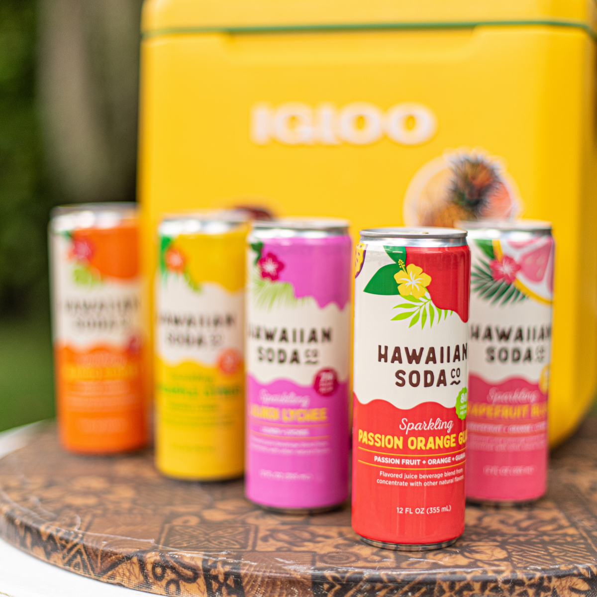 Five cans of Hawaiian Soda Co. on a wooden surface with a yellow cooler in the background.