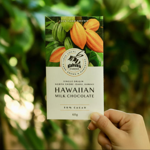 Hand holding a package of Kahuku Farms Hawaiian Milk Chocolate with a blurred green background