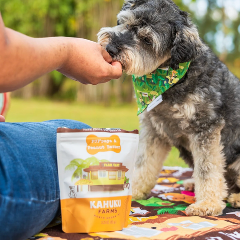 Dog being fed by a person with a Kahuku Farms bag in the foreground