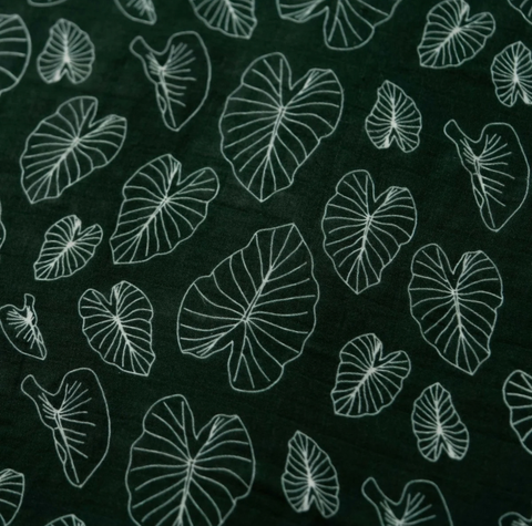 Dark green fabric with a repeating pattern of white outline tropical leaf shapes, likely a cotton or linen textile.