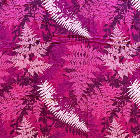 A close-up of a batik fabric featuring a vibrant magenta and pink background with a repeating fern leaf pattern in white and dark magenta.