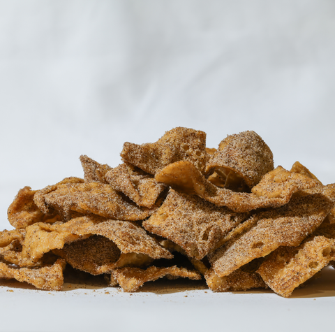 A pile of golden-brown, curled chip-like snacks coated in a fine brown sugar mixture, set against a clean white background.
