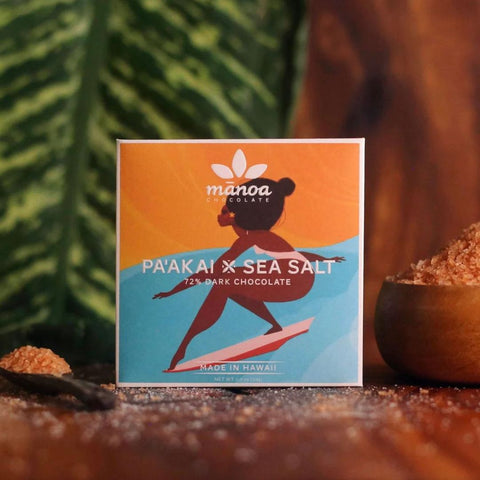 Manoa Chocolate Pa'akai x Sea Salt packaging with a surfboarder design on a wooden surface.