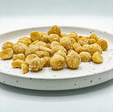 A pile of golden-yellow, sugar-coated candied nuts or macarons arranged on a white speckled ceramic plate against a clean white background.