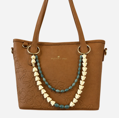 A brown faux-leather handbag with embossed floral detailing, featuring a decorative double strap made of cream flower-shaped beads and blue-green beads, with gold-tone hardware. The brand name 'OCEANS END' is printed in gold on the front.