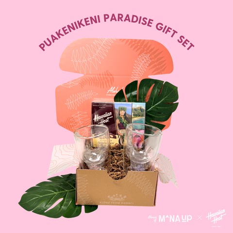 Puakenikeni Paradise gift set with pink box, glasses, and tropical leaves on a pink background