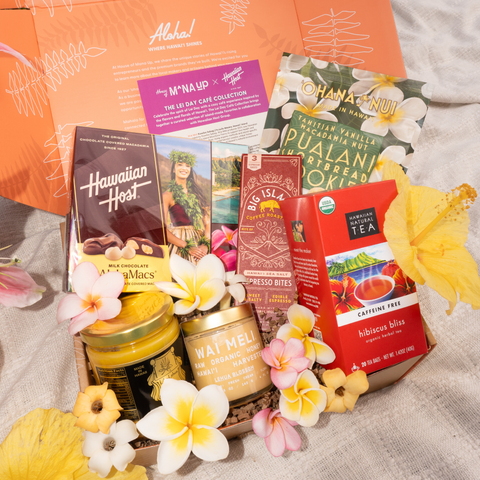 Collection of Hawaiian-themed products including candles, tea, and snacks with floral decorations on a textured surface.