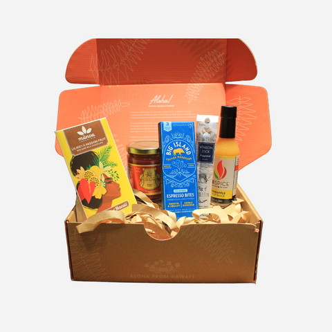 A gift box open to reveal various food items including espresso bites, a pineapple hot sauce, a venison peppered stick, a passion fruit bar, and guava butter.